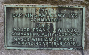 Photo of Detail of the plaque on the north side of the Governor's Foot Guard Boulder Monument #001. Plaque inscription: 1771 / CAPTAIN SAMUEL WYLLYS / COMMANDER / 1912 / MAJOR FRANK L WILCOX / COMMANDING ACTIVE COMPANY / MAJOR WILLIAM J PIERCE / COMMANDING VETERAN CORPS ; 1771 MEMORIAL 1912 / TO THE DECEASED MEMBERS OF / THE FIRST COMPANY GOVERNORS FOOT GUARD / HARTFORD CONNECTICUT / ERECTED BY THE VETERAN CORPS / DEDICATED JUNE 1912